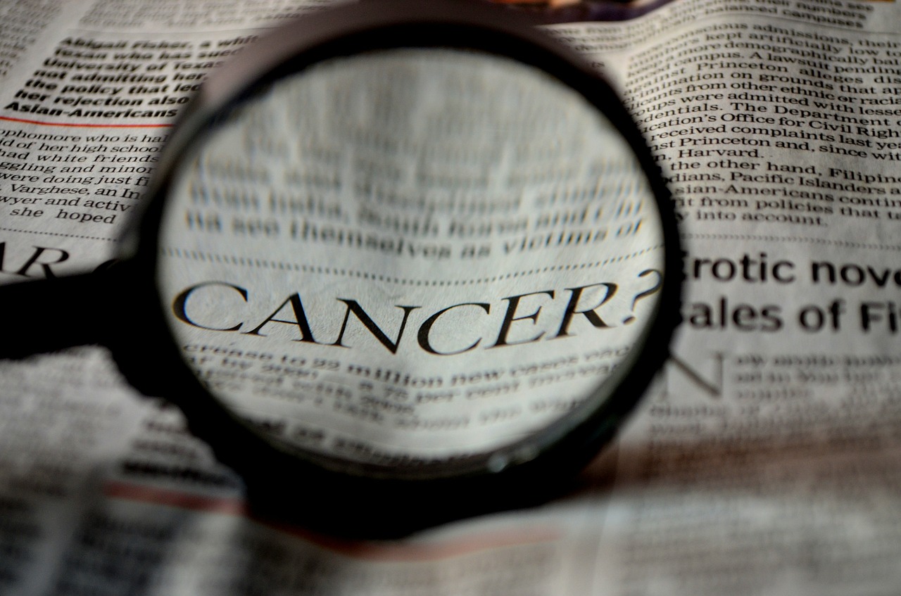 Bild på ett förstoringsglas som pekar på ordet cancer i en tidning