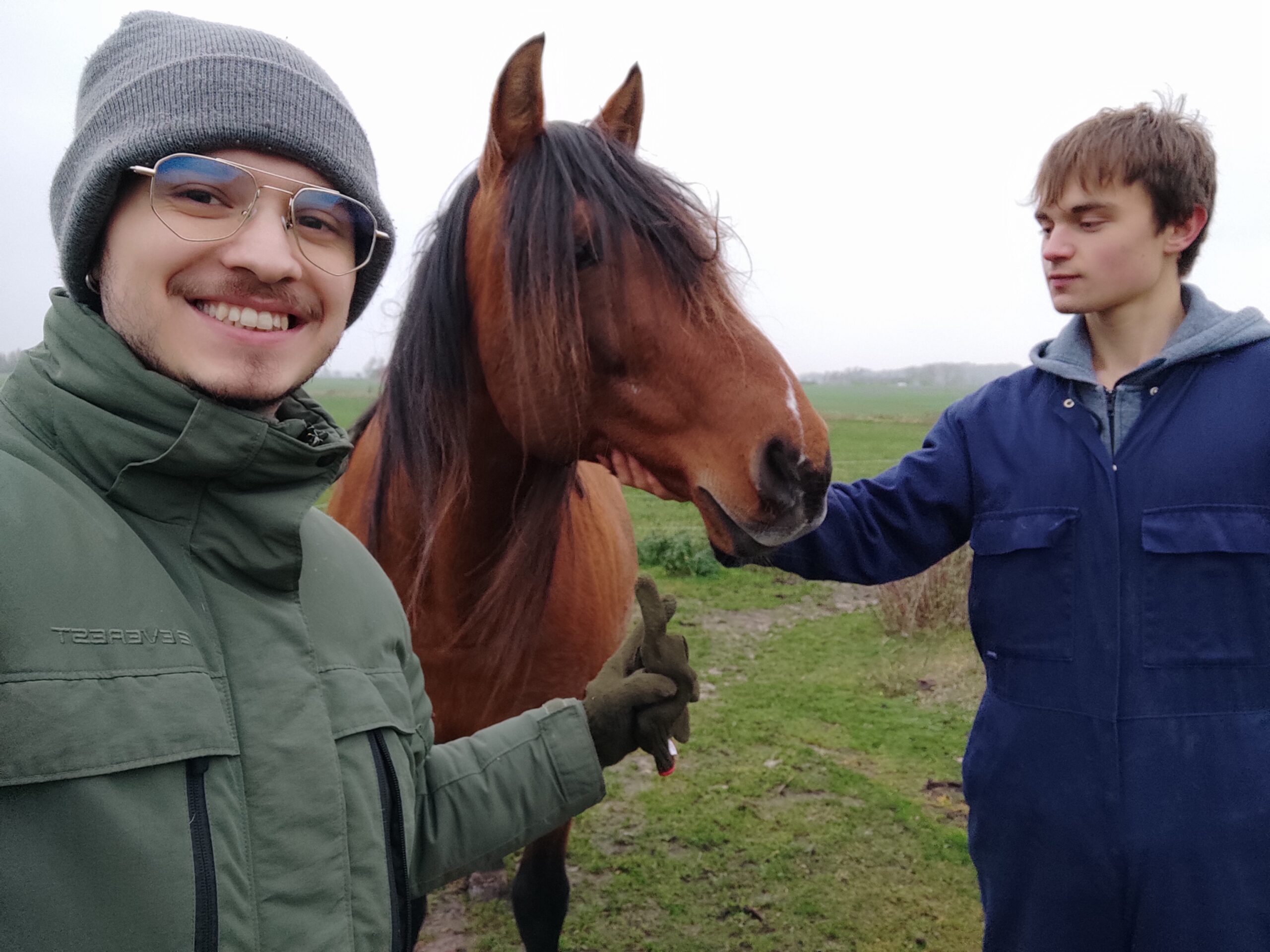 Två unga som står vid och klappar en häst ute i naturen